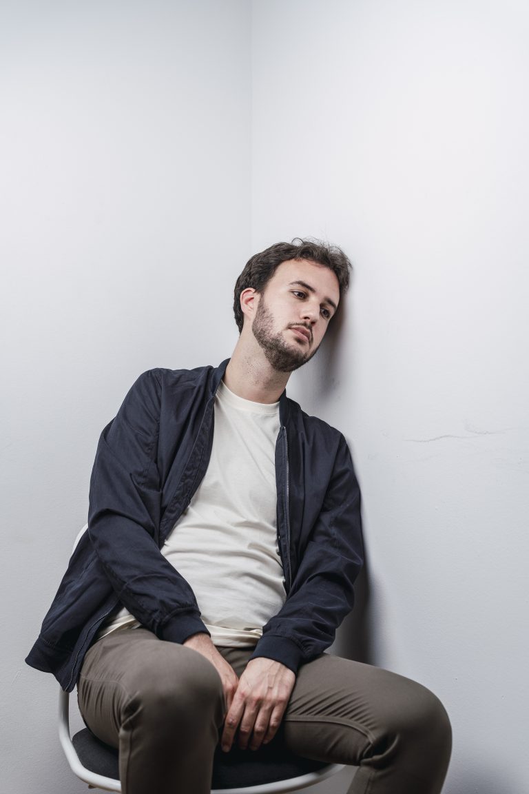 depressed young spanish male sitting chair leaning his head against wall